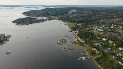 Aerial View of Coastal Town Near Str&ouml;mstad, Sweden with Waterfront Houses, Rocky Hills, Docks, and Calm Sea Under Cloudy Skies
