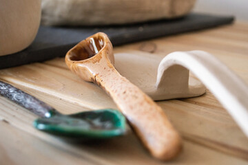 in neat workspace, handcrafted ceramic spoon rests beside clay tools on wooden table. soft natural light highlights textures and details crafts. close up.