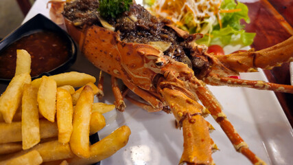 Close-up of a grilled lobster with fries and sauce on a white plate. Delicious seafood dinner with warm lighting, perfect for restaurant menu, advertising or culinary promotion.