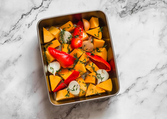 Ingredients for making pumpkin soup - pumpkin, sweet pepper, onion, garlic, thyme, olive oil in a baking dish on a marble background