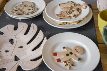 decorative plates hold festive cookies, including gingerbread figures and shapes, arranged on wooden table with tropical leaf design, creating cheerful atmosphere. close up.