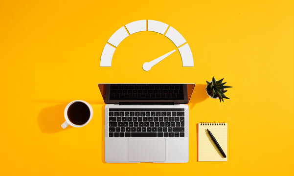 Speedometer with laptop, coffee, notepad and plant on yellow background