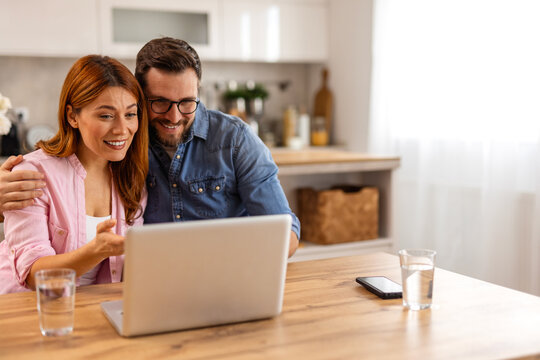 A happy couple working together on a laptop while reviewing documents. They share a moment of collaboration and planning, enjoying a productive and positive atmosphere in their well-lit living space.