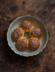 Sweet sesame buns in a baking dish on a wooden table, top view
