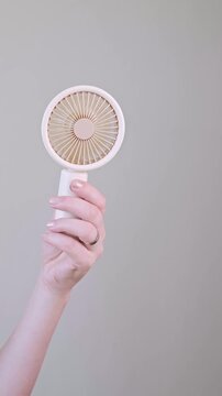 Smiling young woman staying cool with a portable fan while enjoying a warm summer day outdoors.