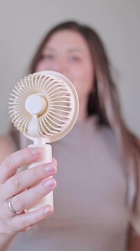 Smiling young woman using a handheld fan for instant relief from the heat on a warm sunny summer day.