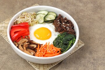 Bibimbap is a Korean dish in the form of a bowl of white rice topped with side dishes of vegetables, beef, eggs and spicy gochujang sauce.