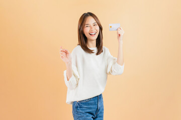 Cheerful beautiful Asian woman holding credit card isolated on beige color background.
