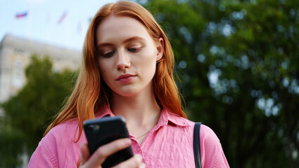 Young woman with red hair looking at phone outdoors image