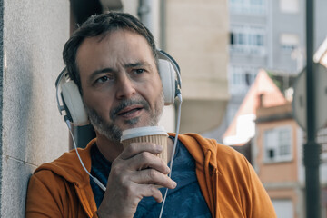 Middle aged man wearing headphones on the street drinking coffee