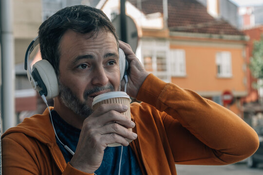 Middle aged man wearing headphones on the street drinking coffee