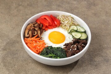 Bibimbap is a Korean dish in the form of a bowl of white rice topped with side dishes of vegetables, beef, eggs and spicy gochujang sauce.