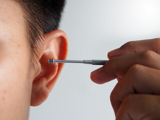 Young person ear with metal ear pick being held by hand offering gentle cleaning sensation and focused self care routine