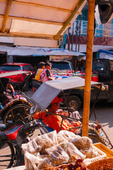 relaxed moment at a traditional Cirebon market: a rickshaw driver pausing beside a spice seller’s booth. weathered textures of the street, intimate glimpse into local livelihoods.