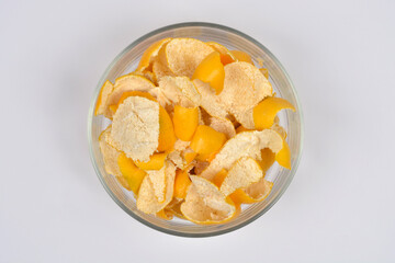 An overhead shot captures a clear glass bowl filled with small pieces of yellow mandarin peel that have been roughly peeled, resting on a clean, white background