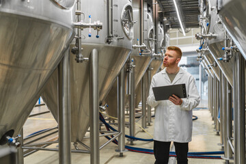 Brewery worker inspecting stainless steel fermentation tanks, upholding quality control standards during beverage production