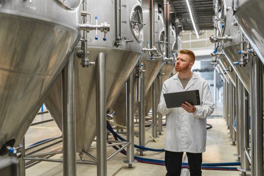 Brewery worker inspecting stainless steel fermentation tanks, upholding quality control standards during beverage production