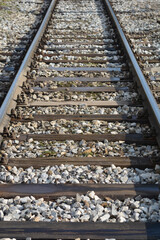 Naklejka premium A straight section of railroad tracks extends into the distance, featuring metal rails, wooden sleepers, and bright gravel ballast in a close-up perspective