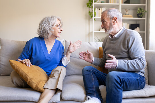 Senior couple arguing and gesturing on sofa at home