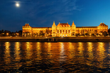 The Budapest University of Technology and Economics glows under the night sky, reflected in the Danube River