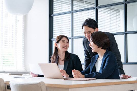 社内でパソコンを見て話をするスーツを着た男女