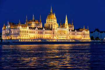 The Hungarian Parliament Building shines brightly at night, its golden lights reflecting in the Danube River