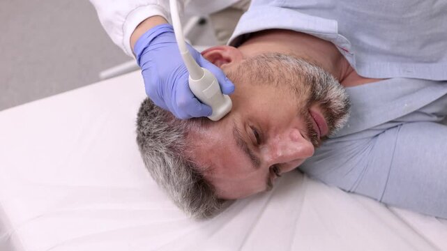 Experienced ultrasound specialist carefully analyzes structure of neck vessels of handsome patient using modern sonographic device in hospital