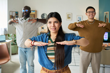 Multiethnic group of adults standing indoors performing synchronized arm exercises, Hispanic woman in foreground leading activity, Black man and Asian man following movement
