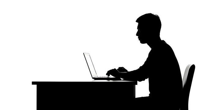 Focused silhouette of a young man typing on a laptop at a desk in a bright, minimalist setting.