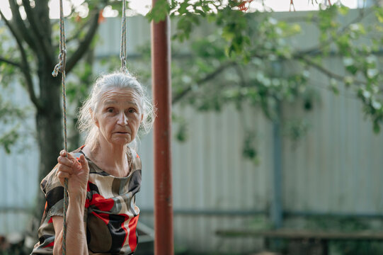 Grandmother sitting on a swing outside in the garden looking at camera