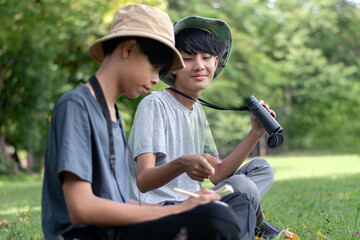 Fototapeta premium Two young explorers collaborate in the field, one observes with binoculars while the other documents the sighting in a notebook.