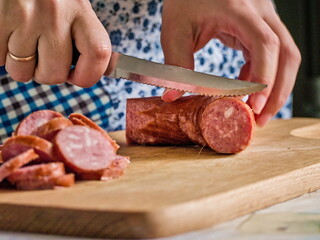 A Woman in an Apron Slicing Smoked Sausage on a Wooden Cutting Board
