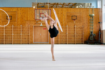 Teenage Caucasian girl performing rhythmic gymnastics routine with hoop on indoor gymnasium floor, demonstrating flexibility and balance during athletic practice session