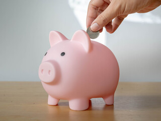 Close-up of a Hands a coin Pink piggy bank on a desk with a jar saving money