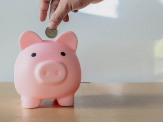 A Hands a coin Pink piggy bank on a desk with a jar saving money
