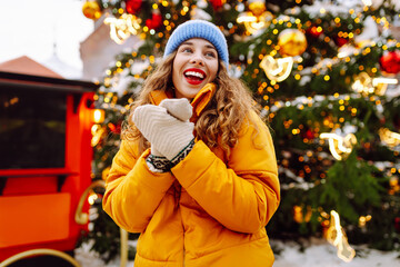 Cheerful woman in yellow jacket enjoys herself at Christmas market on a winter day. A beautiful...