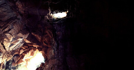 In a deep cave, beams of light penetrate the darkness, illuminating rugged rock formations. The interplay of light and shadow creates a striking natural effect.