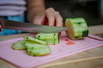 A woman slices a cucumber on a board in a summer kitchen