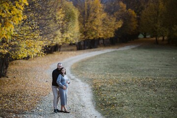 Pregnant couple hugging on autumn path, expecting baby