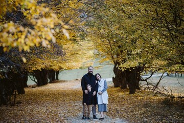 Pregnant family standing on autumn path among yellow leaves
