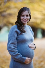 Pregnant woman smiling outdoors holding baby bump