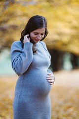 Pregnant woman holding belly smiling outdoors in autumn