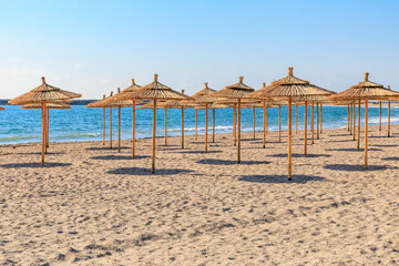 Sandy beach with straw umbrellas by the ocean under clear blue sky