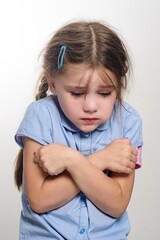 A young girl with a sad expression, arms crossed, looking down.