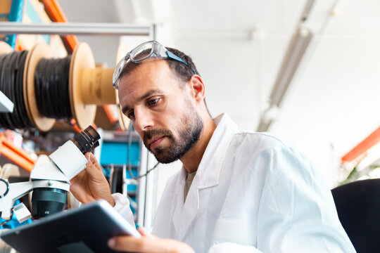 Lab technician inspecting microchip with magnifier in electronics workshop
