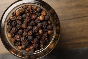 top down flat lay view of whole black pepper in mini glass jar on dark rustic wooden background