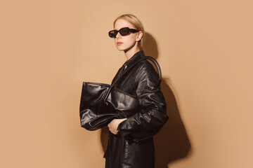Stylish woman in black leather jacket with green shoulder bag in studio