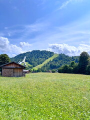 Panorama of a wide road that stretches near a mountain settlement through the hills against the background of a sunny blue, slightly cloudy sky.