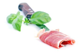 Slice of serrano ham with knife and basil on white background.