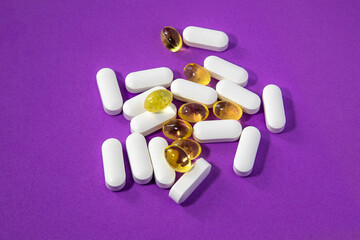 White tablets and yellow gel capsules on vibrant purple background. Medical concept for supplements, vitamins, health care and pharmaceutical ads.